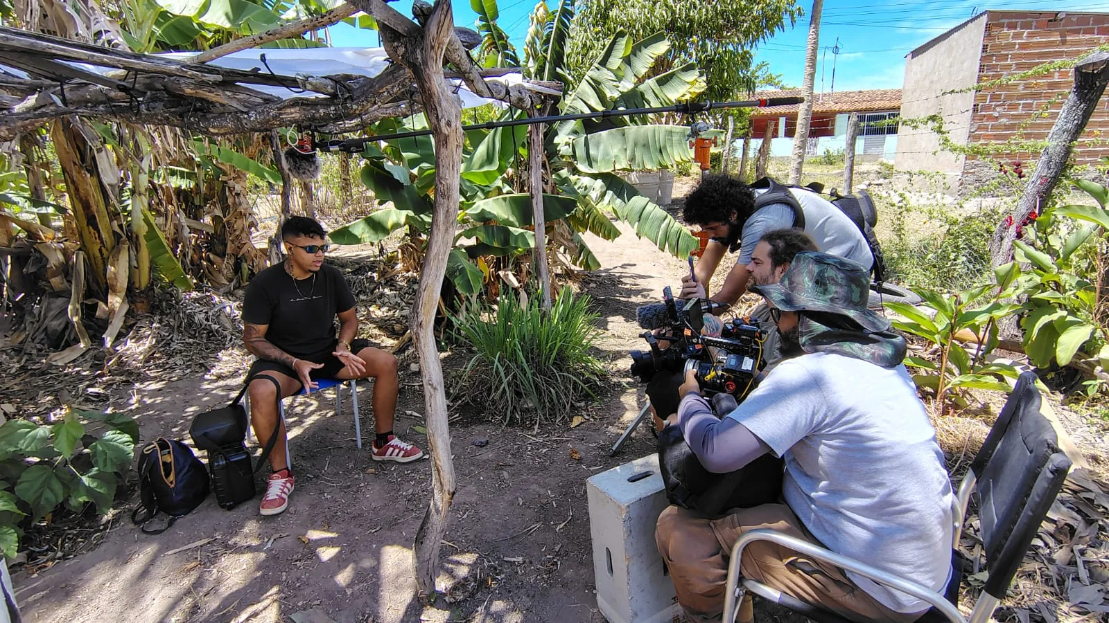 Equipe de filmagem registra uma entrevista ao ar livre, entre bananeiras.