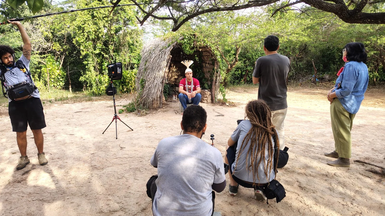 Equipe prepara uma entrevista diante de uma construção tradicional em meio à vegetação.