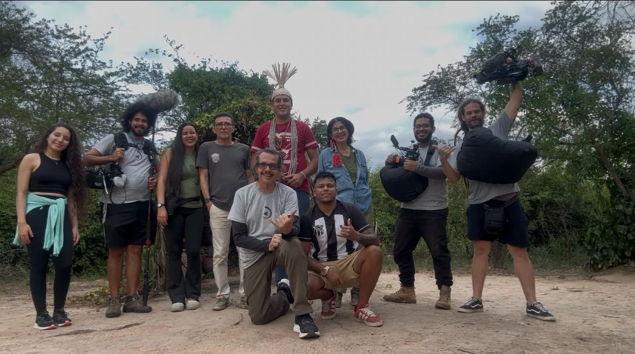 Equipe e participantes posam juntos depois de uma gravação ao ar livre.